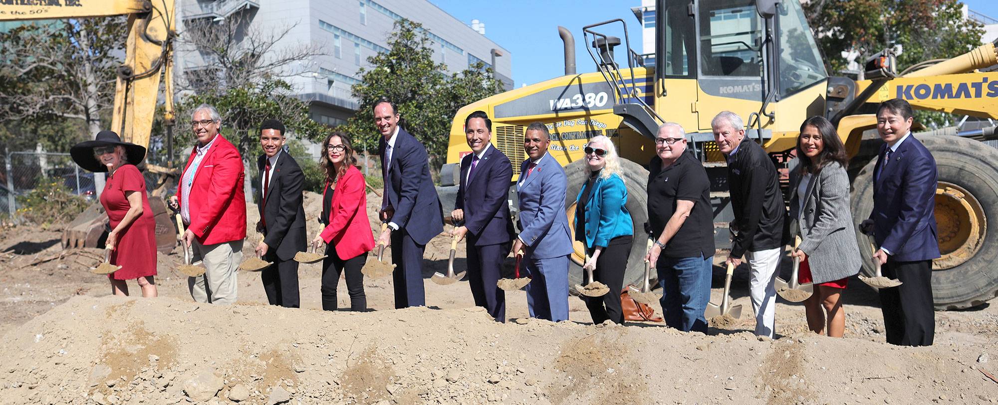 12 people with shovels scoop dirt at a groundbreaking ceremony.