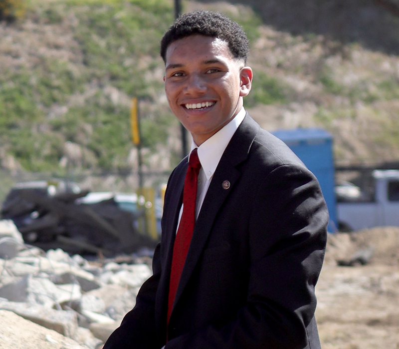 Diego Bethea is outside in a black suit and red tie