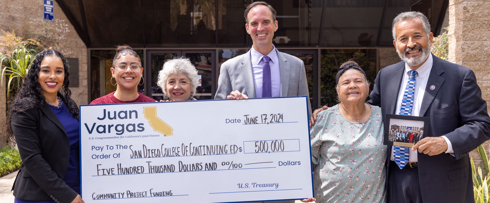 Juan Vargas federal funding Six people hold up a giant check for 500,000 dollars outside of the entrance of the Educational Cultural Complex