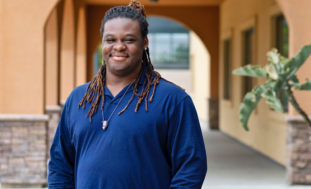 X Ruiz is wearing a dark blue long sleeved sweater. He is outside in front of a building at Miramar College.