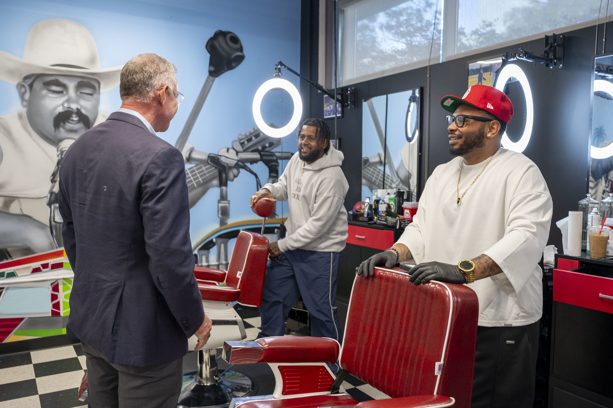 Scott Peters and two barbers stand near red barber chairs