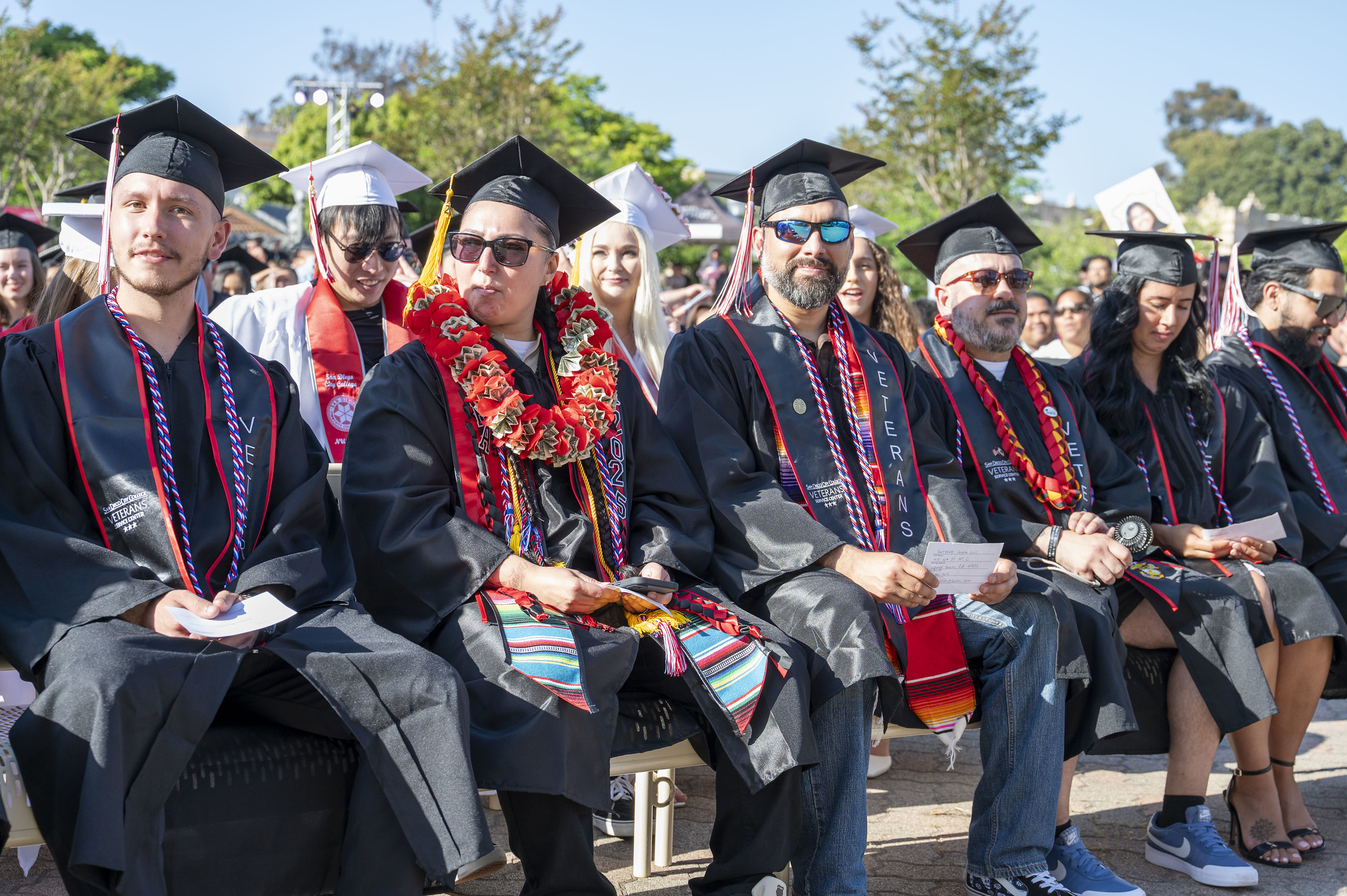 
Six students in black caps and gowns seated during commencement.
