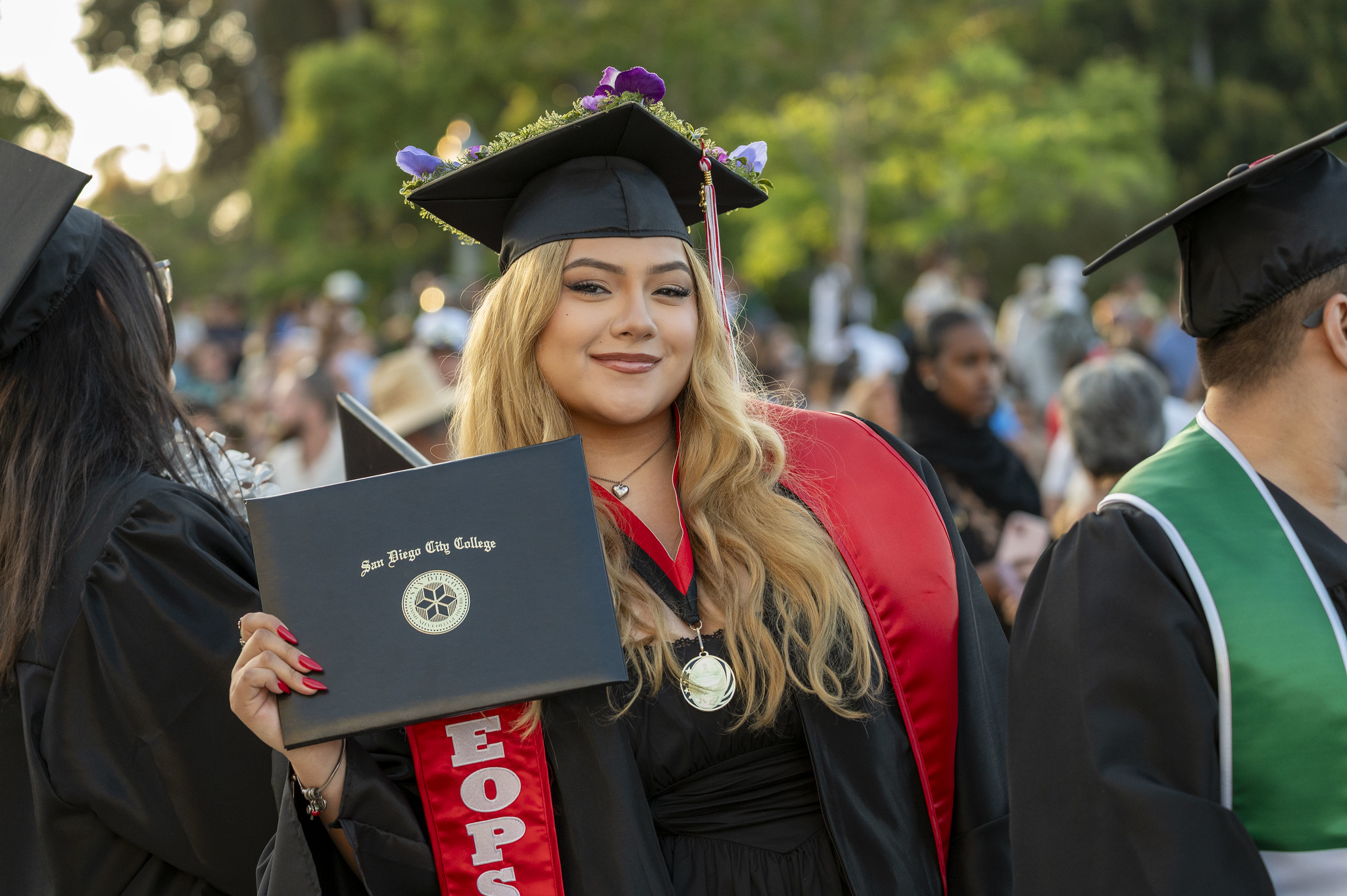 
A graduate is in the audience smiling and holding up her degree.
