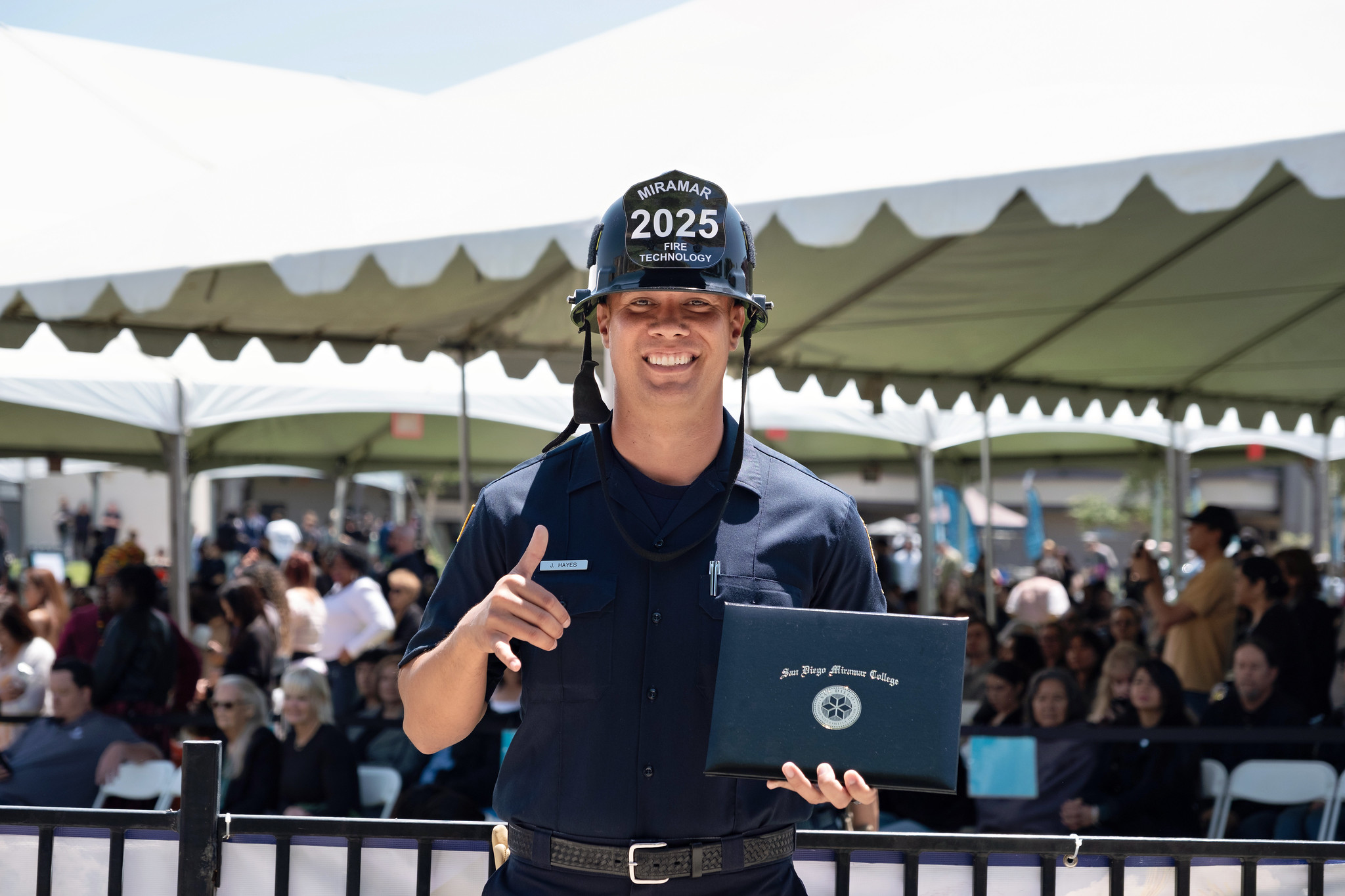 
A fire academy student in a black fire helmet holds up his degree.
