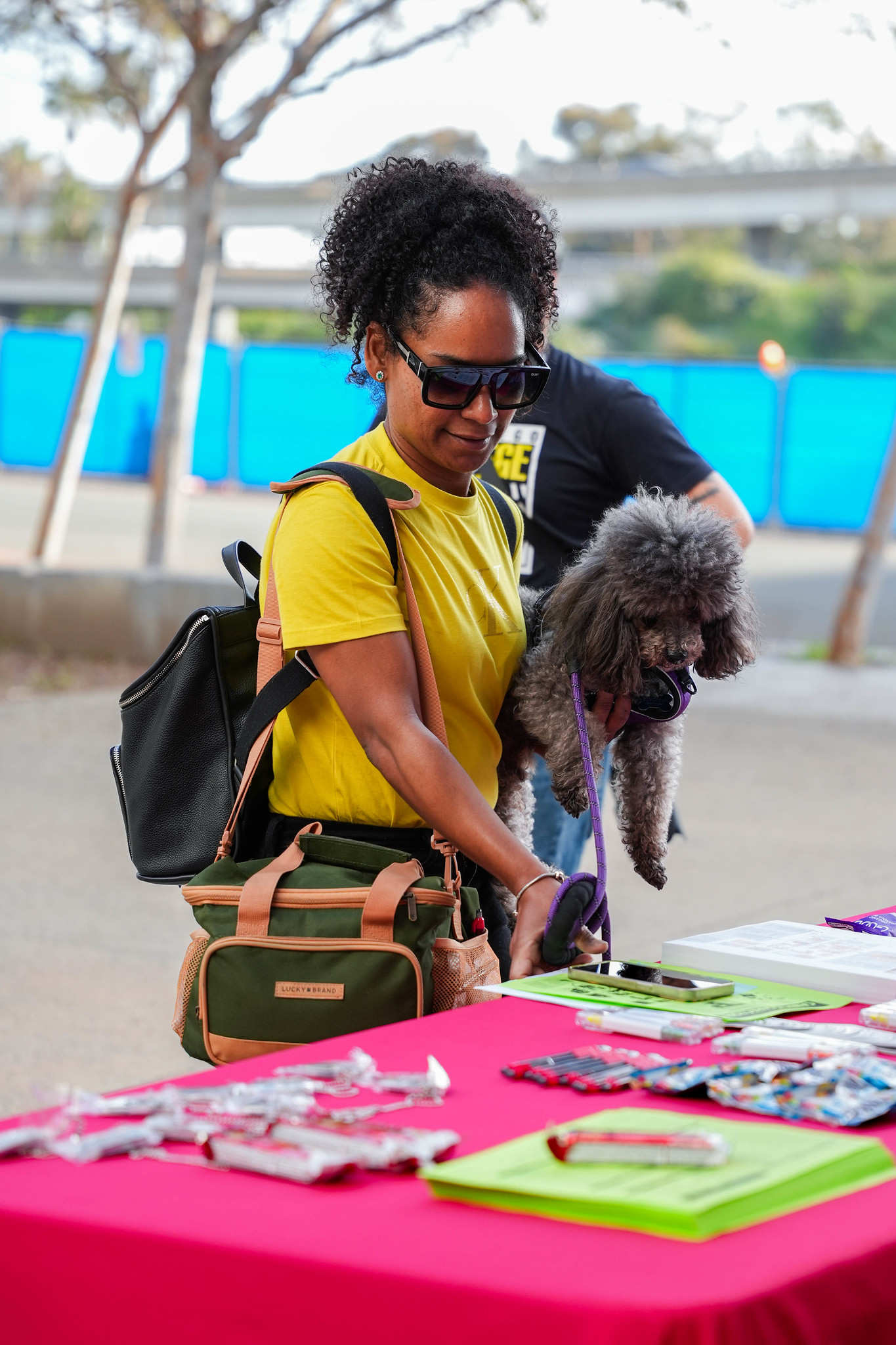 
A lady holding a gray poodle at an information booth.

